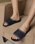 Person wearing navy sandals with a brand logo on a beige armchair.