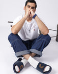 Indoor shot of man wearing Dot Fusion sliders paired with white socks, blue denim, white T-shirt and accesories
