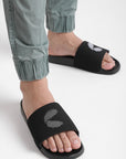 Close-up of black men’s sliders worn with cargo pants, showing the detailed strap texture and contoured footbed in a sleek, all-black finish.