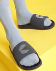 Close-up of navy blue men’s sliders worn with grey socks, foot resting on a yellow surface.