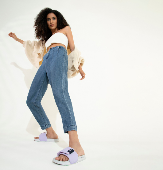 Woman wearing casual streetwear with lilac Chupps slides, styled with high-waisted jeans and a white crop top, showcasing trendy women’s slip-ons.