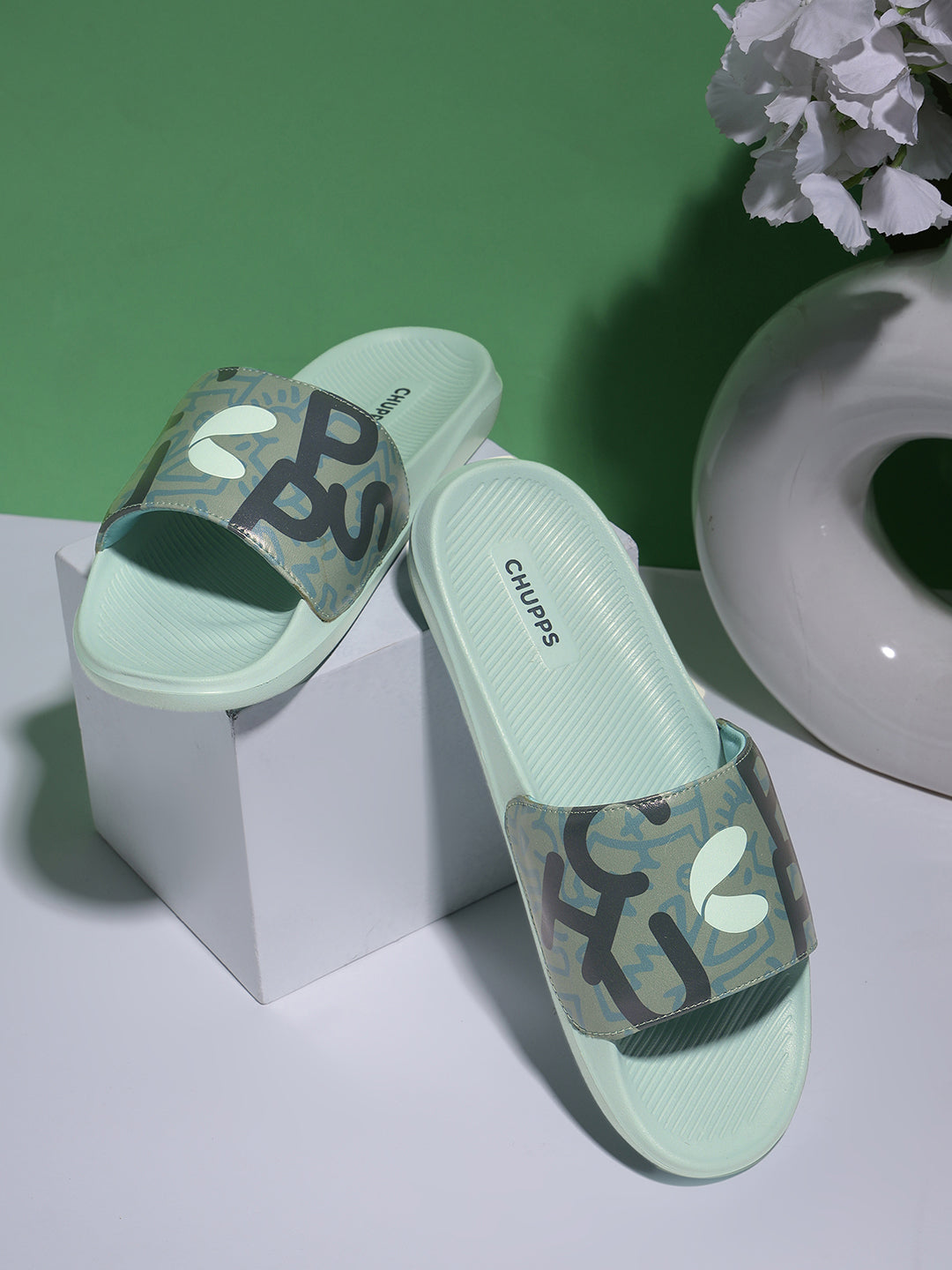 Green slides with camouflage pattern and brand logo on a white and green background .Modern men’s green sliders with graphic upper .