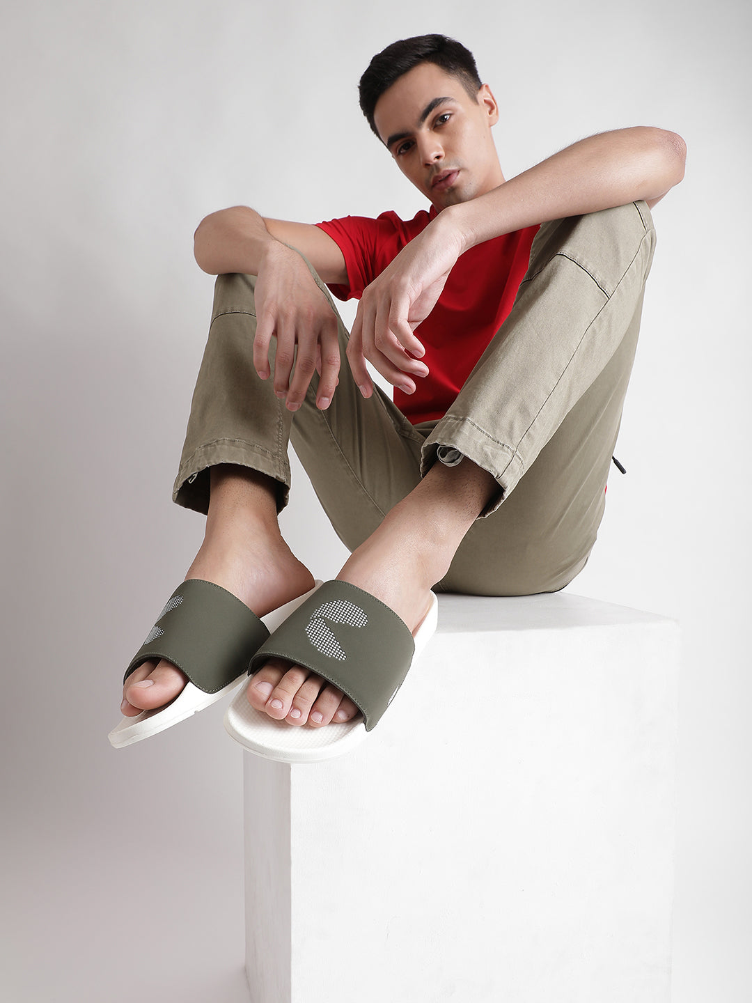 A young man pairs white and olive men’s sliders with cargo pants and a solid red T-shirt, creating a bold yet relaxed casual look.